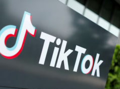 Albania prohíbe TikTok durante un año tras el asesinato de un adolescente Logo de TikTok en un cartel negro ubicado al aire libre, con un fondo difuminado de árboles y un edificio.