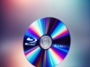 Sony anuncia el fin de la producción de discos Blu-ray, MiniDiscs y cassettes MiniDV en febrero de 2025 Un disco Blu-ray en primer plano, con un diseño brillante y colorido que refleja tonos vibrantes de azul, rojo, amarillo y verde sobre una superficie pulida. El logotipo de "Blu-ray" es claramente visible en el disco, destacando su característico estilo. El fondo es desenfocado, con un efecto de iluminación suave y tonalidades cálidas y frías que crean un ambiente moderno y nostálgico.