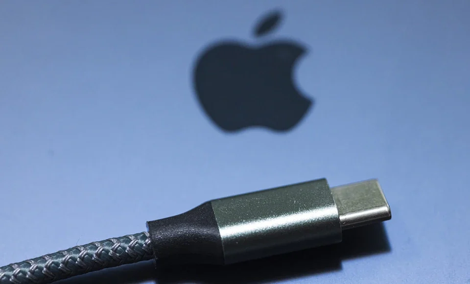 Cargadores Móviles UE Cable USB-C con diseño trenzado en primer plano, colocado sobre una superficie gris con el logotipo de Apple difuminado al fondo.