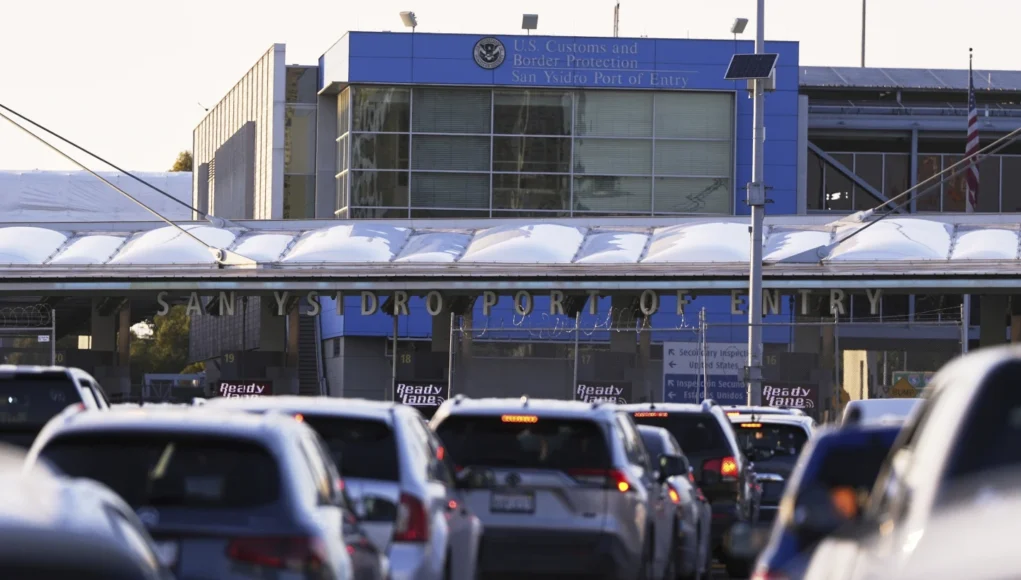 Vehículos en fila esperando cruzar la frontera en el puerto de entrada de San Ysidro, con el edificio de la Oficina de Aduanas y Protección Fronteriza de Estados Unidos al fondo.