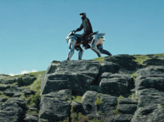 Kawasaki presenta un caballo robot a hidrógeno que se montará en el futuro Persona montando un vehículo robótico cuadrúpedo de aspecto futurista sobre una formación rocosa al aire libre. El robot, con diseño metálico y articulaciones visibles, simula la forma de un animal de cuatro patas, mientras el piloto lleva casco y vestimenta de protección bajo un cielo despejado.