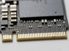 China crea la memoria flash más rápida del mundo: 25 mil millones de bits por segundo Vista en primer plano de una unidad de estado sólido (SSD) con interfaz NVMe, mostrando los conectores dorados y componentes electrónicos sobre una placa de circuito negro.