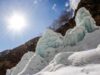 Glaciares artificiales impulsan el suministro de agua en el norte de Pakistán Formaciones de hielo y nieve en una ladera montañosa bajo un cielo despejado, con el sol brillando intensamente y árboles sin hojas al fondo, creando un contraste entre el clima frío y la luz solar.