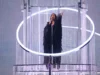 Escándalo en Eurovisión: ¿Activismo, hacking o campaña de blanqueamiento? La polémica tras el voto popular Mujer cantando con un micrófono en una plataforma elevada rodeada de estructuras circulares y decoraciones brillantes, bajo una iluminación escénica intensa.