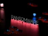 Descubren un malware que opera sin internet y se autodestruye en segundos Palabra 'RANSOMWARE' iluminada sobre un fondo oscuro con una rejilla digital y luces rojas y azules.
