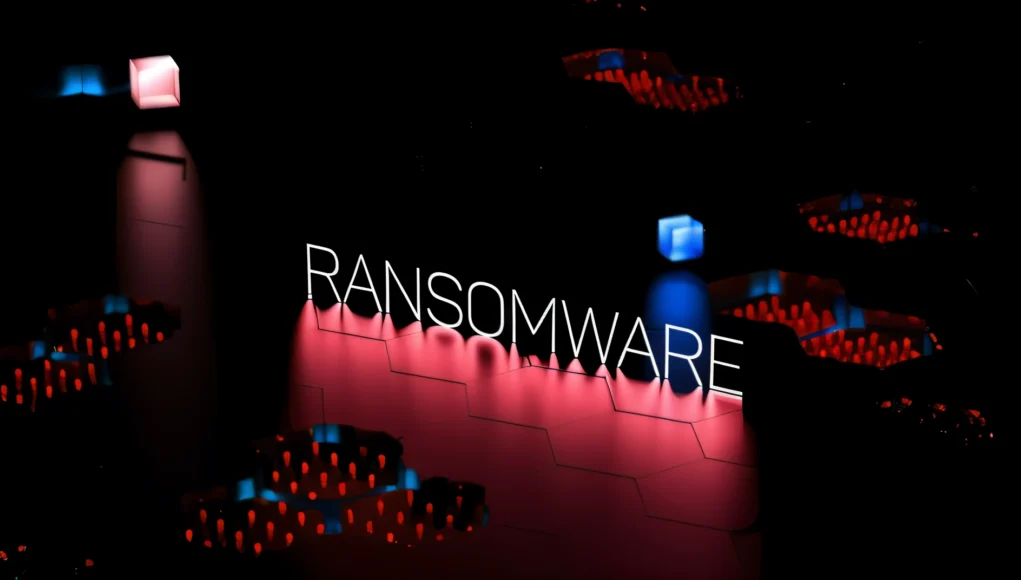 Palabra 'RANSOMWARE' iluminada sobre un fondo oscuro con una rejilla digital y luces rojas y azules.