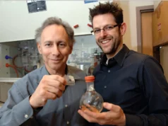 MIT desarrolla vendaje médico inspirado en geckos para cirugías Dos personas en un laboratorio posan para la cámara. La persona a la izquierda sostiene un pequeño cuadrado translúcido que parece un material experimental, mientras que la persona a la derecha sostiene un matraz esférico con tapón naranja. Al fondo se observan equipos y mobiliario de laboratorio, incluyendo una campana extractora.