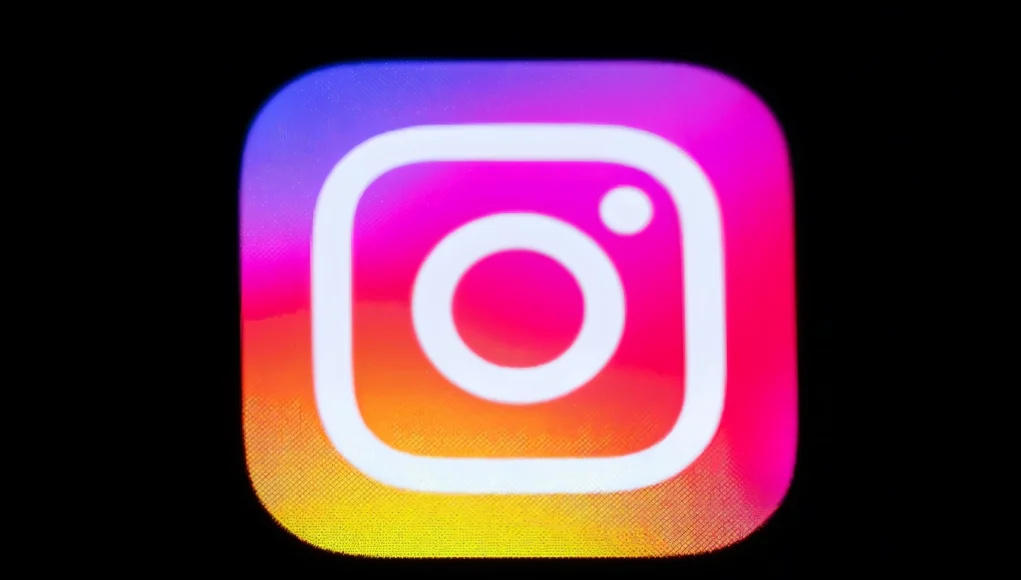 Logotipo de la aplicación Instagram en primer plano, con su característico fondo degradado en tonos rosados, naranjas y violetas, acompañado del nombre “Instagram” en texto blanco sobre fondo negro.