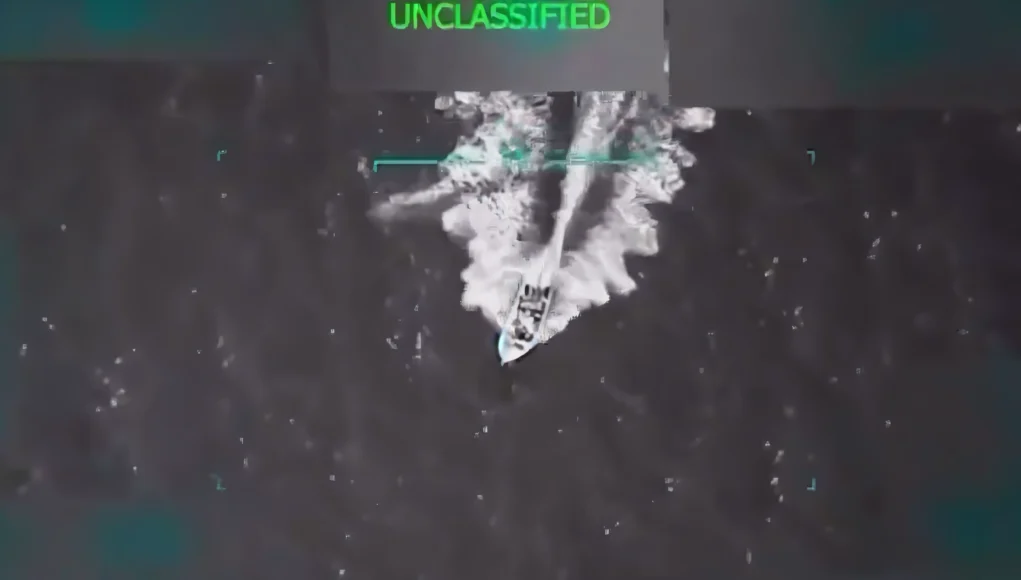 Imagen aérea en blanco y negro de una lancha rápida navegando a alta velocidad sobre el mar, capturada desde una cámara de vigilancia con interfaz de seguimiento. En la parte superior de la imagen aparece la palabra “UNCLASSIFIED” en verde, indicando que el contenido no es clasificado.