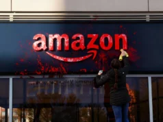 Amazon despide a ingeniero palestino que protestó contra contrato militar con Israel Persona limpiando un cartel de Amazon que ha sido manchado con pintura roja, usando un trapo y un spray limpiador.