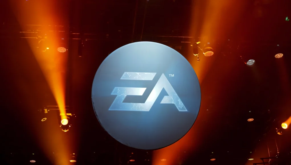 Logotipo de Electronic Arts (EA) iluminado en un escenario oscuro con focos naranjas apuntando hacia arriba.