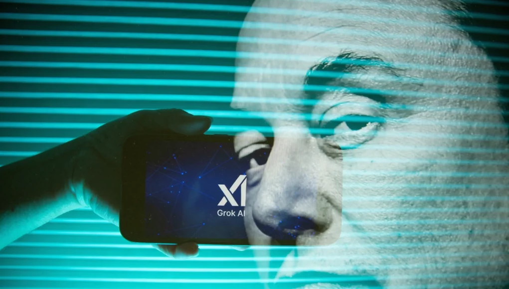 Mano sosteniendo un móvil con el logo de Grok AI sobre un fondo digital azul verdoso, mientras se proyecta en segundo plano el rostro de un hombre, parcialmente superpuesto por líneas horizontales de luz.