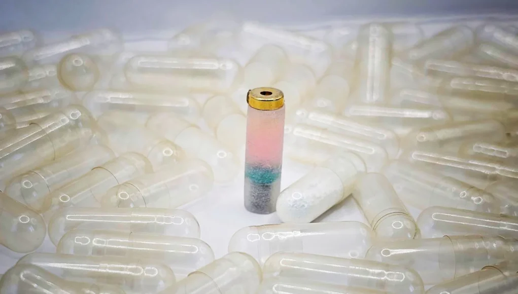 Cápsula médica experimental con sensores de colores en su interior, diseñada para monitorear el sistema digestivo, rodeada de cápsulas transparentes vacías.