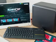 Casi el 90 % de los juegos de Windows ya funcionan en Linux Un pequeño setup de escritorio con monitor mostrando Steam y el juego RoboCop: Rogue City, acompañado de un teclado inalámbrico y un ordenador compacto sobre una mesa de madera.