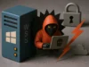 Explotación activa de vulnerabilidad crítica en Windows Server WSUS preocupa a expertos y gobiernos Un hacker con sudadera roja y capucha que emerge de un servidor azul con el logo de Windows y las siglas WSUS. El personaje utiliza un portátil gris con una calavera negra en la tapa. A su alrededor aparecen un candado gris, un rayo naranja y una nube, simbolizando una vulnerabilidad de seguridad en Windows Server Update Services.
