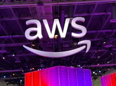 AWS invierte 50 mil millones de dólares para construir infraestructura de IA exclusiva para el gobierno de Estados Unidos Gran cartel iluminado con el logo de AWS suspendido del techo en un recinto interior, con luces moradas y estructuras metálicas visibles en el fondo.
