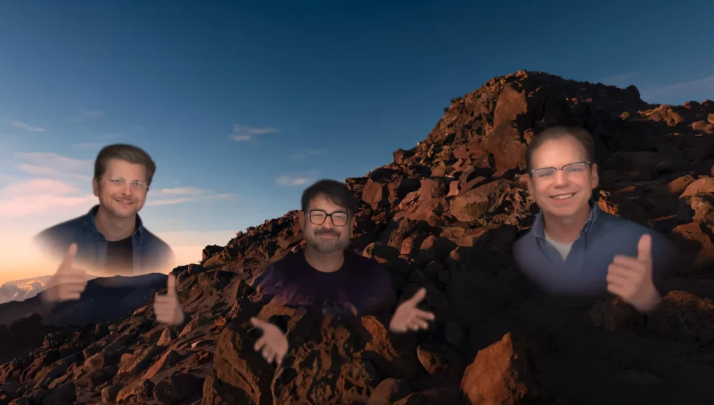 Tres avatares semitransparentes de hombres aparecen sobre un paisaje rocoso al atardecer; los tres están sonriendo, dos de ellos levantan los pulgares y el del centro gesticula con las manos.