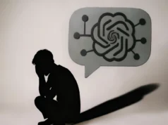 Familias denuncian que los últimos momentos de sus seres queridos fueron con inteligencia artificial en lugar de humanos Silueta oscura de una persona sentada en el suelo, encorvada y con la cabeza entre las manos en señal de angustia. Frente a ella aparece un gran bocadillo de conversación gris con el logotipo estilizado de una inteligencia artificial y pequeñas conexiones a su alrededor, proyectando una sombra alargada. La escena es minimalista y transmite soledad, dependencia emocional y reflexión sobre la inteligencia artificial.