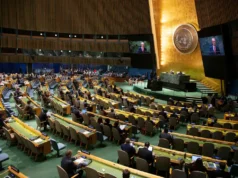 ¿Deberíamos celebrar la Convención de la ONU contra el cibercrimen? Lecciones de 25 años luchando contra el crimen transnacional Vista general del salón de la Asamblea General de las Naciones Unidas, con delegados sentados en filas curvadas mientras escuchan un discurso desde el podio central. En el fondo se observa el emblema dorado de la ONU y grandes pantallas que muestran al orador.
