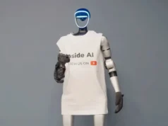 Robot humanoide dispara a YouTuber tras manipular sus protocolos de seguridad Robot humanoide de aspecto futurista con rostro iluminado en azul, vestido con una camiseta blanca con el texto “Inside AI” y un icono de YouTube, de pie frente a un fondo neutro gris, representando la divulgación y presencia de la inteligencia artificial en medios digitales.