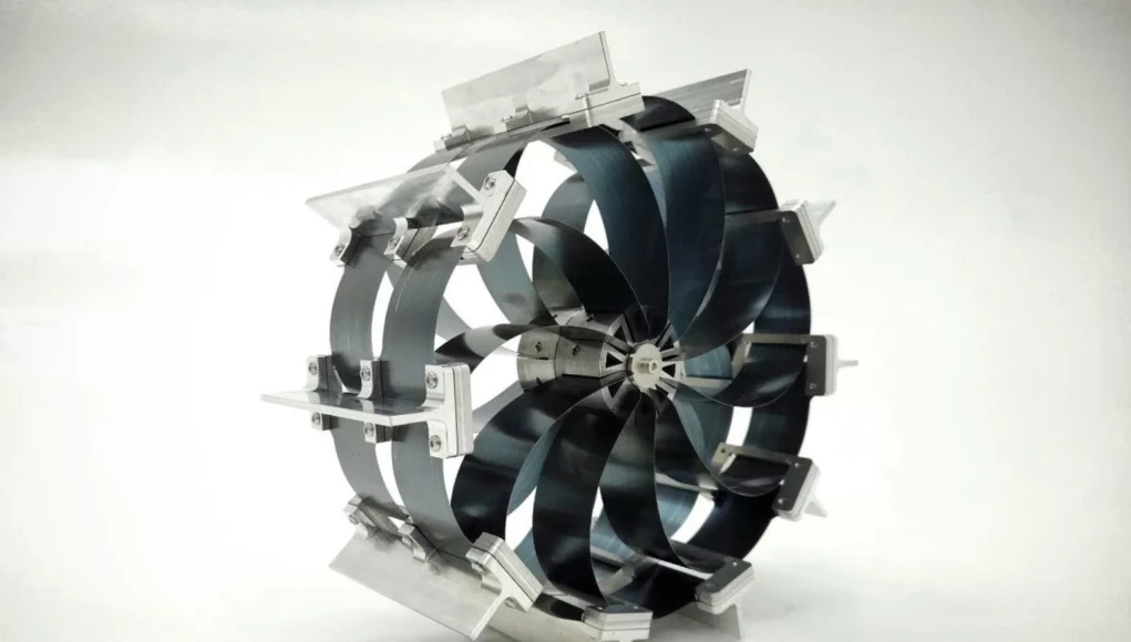 Dispositivo mecánico circular con múltiples palas curvadas montadas en una estructura metálica, diseñado como una rueda o turbina experimental, fotografiado sobre un fondo blanco.