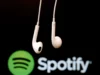 Grupo activista afirma haber extraído 86 millones de archivos musicales de Spotify Auriculares blancos con cable suspendidos frente al logotipo de Spotify desenfocado sobre fondo oscuro, evocando el consumo de música y audio en plataformas digitales.
