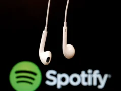 Grupo activista afirma haber extraído 86 millones de archivos musicales de Spotify Auriculares blancos con cable suspendidos frente al logotipo de Spotify desenfocado sobre fondo oscuro, evocando el consumo de música y audio en plataformas digitales.